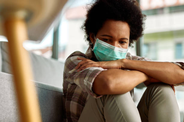 Quarantine anxiety! Sad African American woman wearing face mask while sitting at home and thinking of something. anxiety stock pictures, royalty-free photos & images