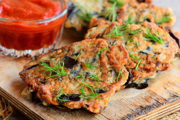 Quick and easy eggplant cutlets. Fried eggplant cutlets with garlic and dill on a wooden board. Tomato sauce in a glass bowl. Healthy veggie recipe. Closeup stock photo