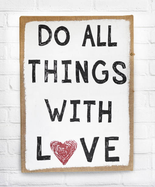 Quote do all things with love text on hanging sign board against white brick wall stock photo