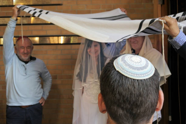 Rabbi belssing Jewish bride and a bridegroom under a chupa Rear view of a Rabbi belssing Jewish bride and a bridegroom under a chupa (canopy made out of tallit that represents a Jewish home) in a synagog a on their wedding day after Conversion to Judaism. chupah stock pictures, royalty-free photos & images