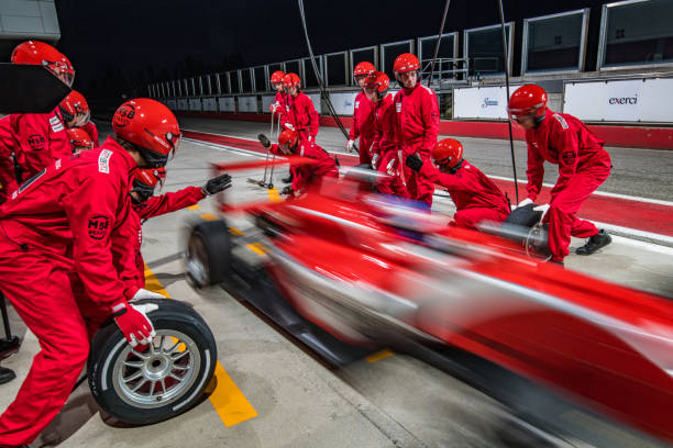 Racing team working at pit stop Pit crew in red uniforms changing tires on formula race car during pit stop. sports team stock pictures, royalty-free photos & images