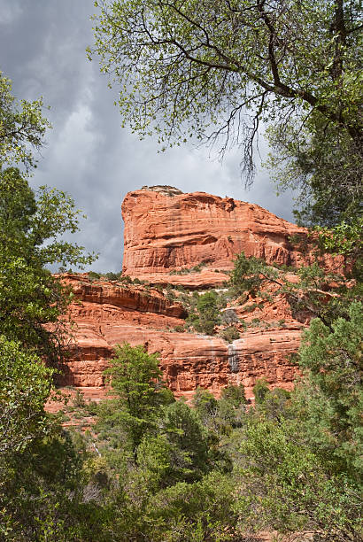 Rain Clouds Over a Red Butte Greater Sedona and the Verde Valley are areas of uncommon beauty and diversity in the desert of Northern Arizona. It is known for its wide-open vistas, red-rock buttes, steep wooded canyons, pine forests and riparian corridors. Nearby Oak Creek, West Fork and the Verde River provide cool green shade in the spring and summer and a kaleidoscope of color in the fall. Much of this region is within the Coconino National Forest which includes several designated national wilderness areas. This scene of red rock and contrasting green trees was photographed at Boynton Canyon in the Red Rock Secret Mountain Wilderness near Sedona, Arizona, USA. jeff goulden sedona stock pictures, royalty-free photos & images