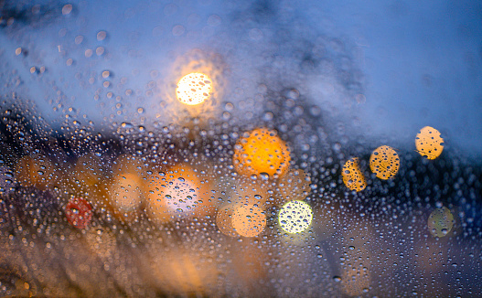 Abstract, close up of raindrops on windshield with street light at night.