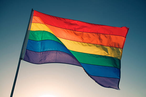 Rainbow Gay Pride Flag Waving Backlit by Bright Sun Sky stock photo