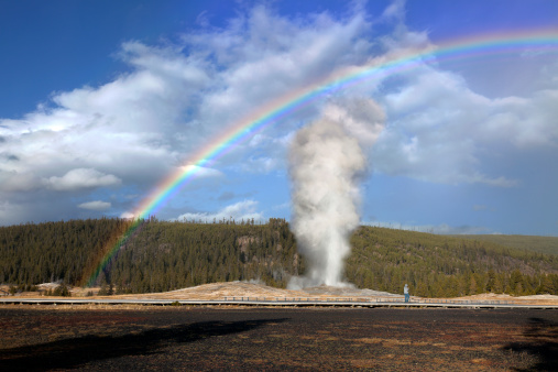 Old Faithful is a cone geyser located in state of Wyoming, Yellowstone National Park in the United States. It is erupting on average every ninety minutes. Full rainbow appeared when the rainstorm passed by.