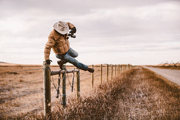 Rancher jumps over barbed wire fence to get to road Ranching worker jumps over barbwire fence while holding binoculars in order to get to back road. rancher stock pictures, royalty-free photos & images
