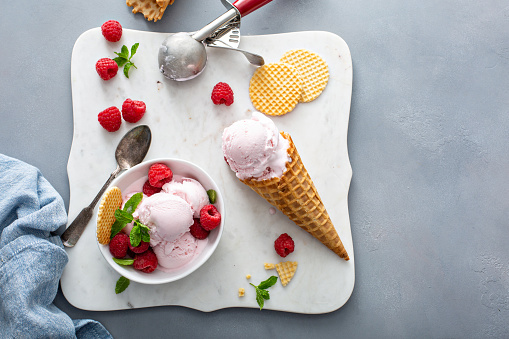 Raspberry ice cream in a bowl and waffle cone with fresh berries