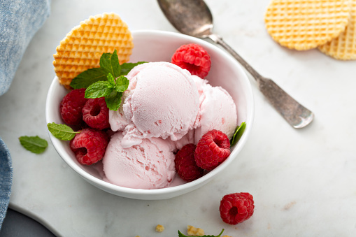 Raspberry ice cream in a bowl with fresh berries and waffle
