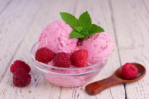 Raspberry ice cream in a transparent glass bowl on a wooden table.