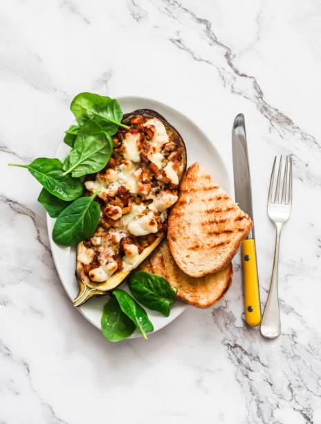 Ratatouille stuffed baked eggplant with mozzarella cheese, spinach and grilled bread on a light background, top view. Delicious vegetarian lunch stock photo