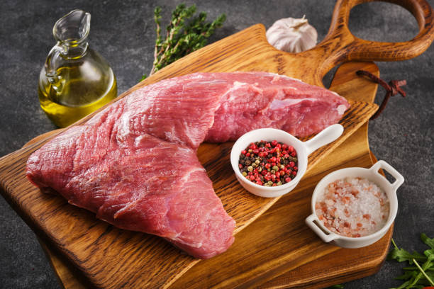 Raw beef tri-tip steak for BBQ on wooden board with salt, garlic and pepper, top view. stock photo