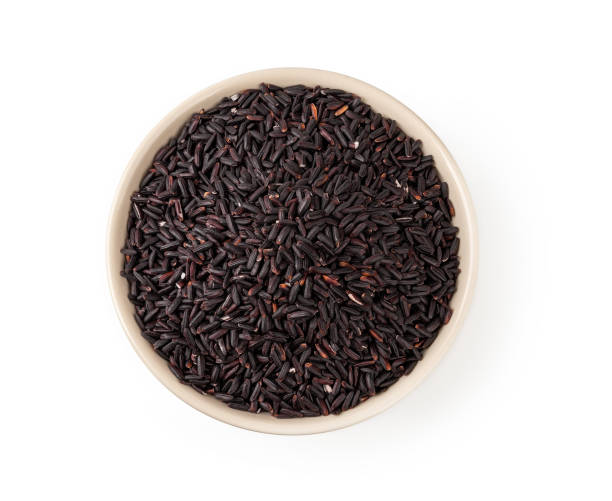 Raw black rice in a beige ceramic bowl isolated on white background. Unpolished organic black rice as source of complex carbohydrates. Ingredient for dieting and healthy eating. stock photo