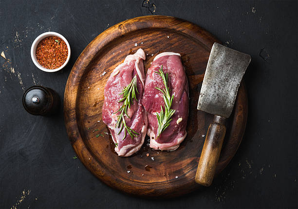 Raw duck breast with rosemary, spices on dark wooden tray Raw uncooked poultry meat cut. Duck breast with rosemary, spices and butcher cleaver on dark wooden tray over black wooden background, top view duck meat photos stock pictures, royalty-free photos & images
