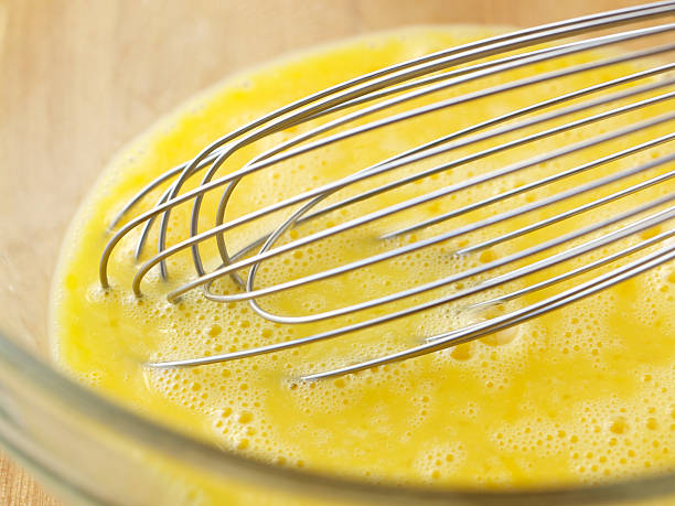 Raw eggs and whisk in glass bowl stock photo