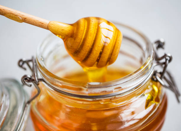 Raw organic honey in a jar with dipper closeup, healthy natural sweetener stock photo