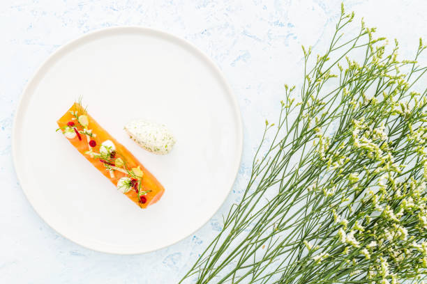 Raw salmon fillet cut topped with apple, beetroot, cream cheese and dill aside a twig with white flowers and a quenelle of cheese and dill over a blue background. stock photo