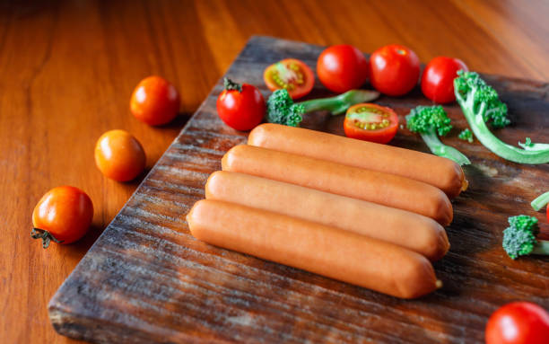 Raw sausage on a wooden cutting board with broccoli and tomatoes stock photo