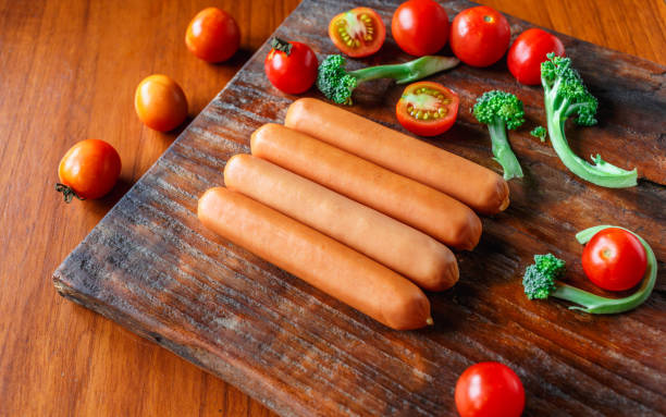 Raw sausage on a wooden cutting board with broccoli and tomatoes stock photo