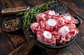 istock Raw veal beef Oxtail Meat on butcher wooden board with cleaver. Dark wooden background. Top view 1306354426