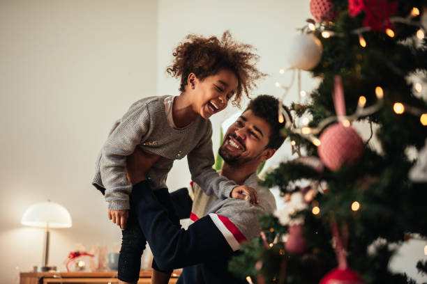 Reaching for the top of the Christmas tree! Shot of an african american father and daughter celebrating Christmas with love at home. decorating stock pictures, royalty-free photos & images