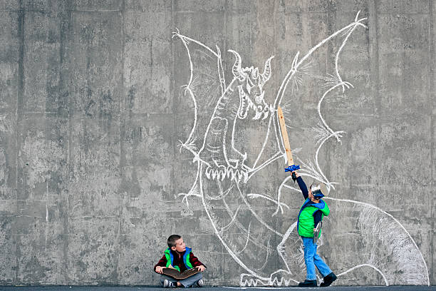 Reader imagination Boy reading a book and imagining himself fighting a dragon. Importance of reading and existence of non-visual media. Dragon chalk drawing on the concrete wall. Natural light. dragon photos stock pictures, royalty-free photos & images