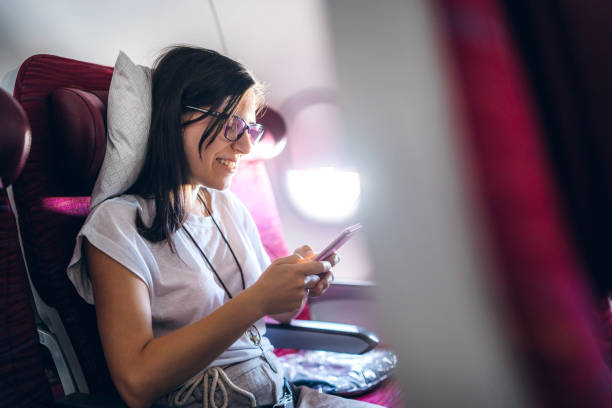 Reading news or messages on an airplane Young beautiful Caucasian woman reading news or messages on smartphone on a airplane. plane window seat stock pictures, royalty-free photos & images