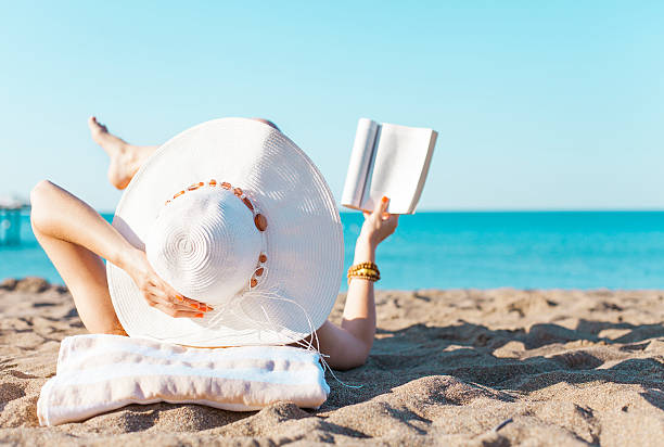 Mujer con gran sombrero de paja lee tumbada en la playa