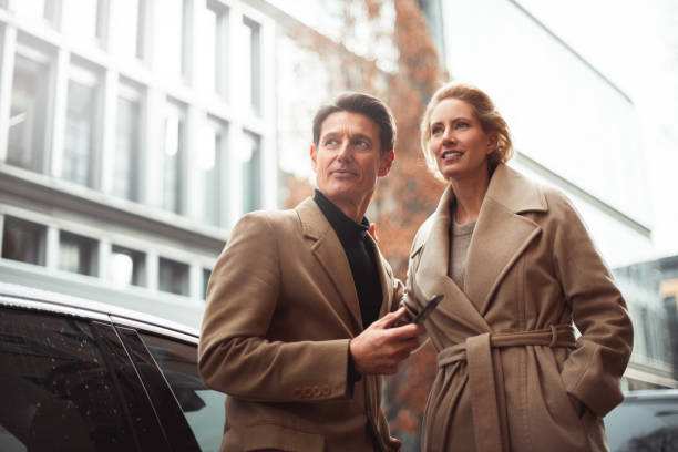 Ready for a trip Smart casual couple is standing next to their car ready to go for a road trip. He is holding a smartphone and both of them are looking at the same point down the street. georgijevic frankfurt stock pictures, royalty-free photos & images