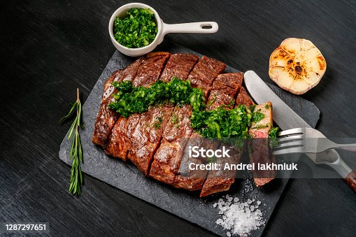 istock Ready to eat black Angus beef rib eye steak sliced with herbs, garlic and sauce on slate Board. Ready meal for dinner on the background of dark ebony. 1287297651