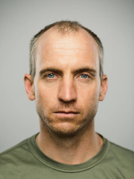 Real caucasian man with blank expression Close up portrait of mature adult adult caucasian man with blank expression against gray background. Vertical shot of real canadian man staring in studio with short balding hair and blue eyes. Photography from a DSLR camera. Sharp focus on eyes. blank expression stock pictures, royalty-free photos & images