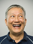 Close up portrait of senior asian man with happy excited expression looking to the side against white gray background. Vertical shot of chinese real people laughing ecstatic from a joke in studio with gray hair. Photography from a DSLR camera. Sharp focus on eyes.