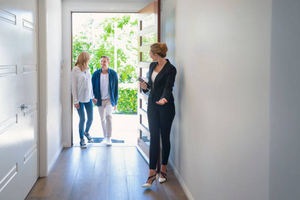 Real estate agent showing a young couple a new house. Real estate agent showing a young couple a new house. The house is contemporary. All are happy and smiling. The couple are casually dressed and the agent is in a suit. The couple are being greeted at the front door by the real estate agent. Copy space model house stock pictures, royalty-free photos & images