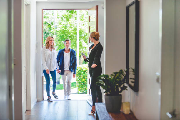 Real estate agent showing a young couple a new house. Real estate agent showing a young couple a new house. The house is contemporary. All are happy and smiling. The couple are casually dressed and the agent is in a suit. The couple are being greeted at the front door by the real estate agent. Copy space real estate agent stock pictures, royalty-free photos & images