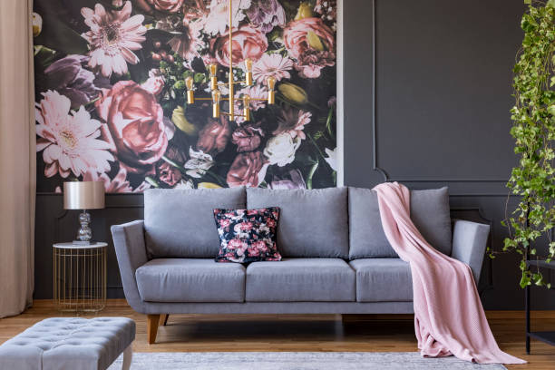 Real photo of a living room interior with a sofa, pillow, blanket and flowers on wallpaper Real photo of a living room interior with a sofa, pillow, blanket and flowers on wallpaper cushion photos stock pictures, royalty-free photos & images
