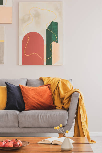 Real photo of an abstract painting hanging on white wall in living room interior with colorful cushions on gray sofa Real photo of an abstract painting hanging on white wall in living room interior with colorful cushions on gray sofa cushion stock pictures, royalty-free photos & images