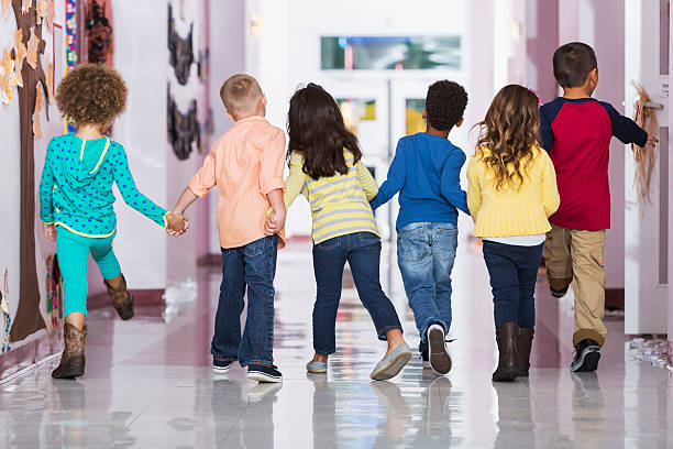 Rear view, group of preschoolers walking down hallway Rear view of a multi-ethnic group of six children holding hands, walking down a school hallway together.  They are in kindergarten or preschool 4 to 6 years old. children only stock pictures, royalty-free photos & images