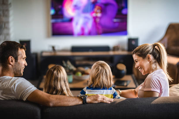 Rear view of a family watching TV on sofa at home. Back view of a happy parents enjoying while watching TV with their kids on sofa in the living room. watching tv stock pictures, royalty-free photos & images