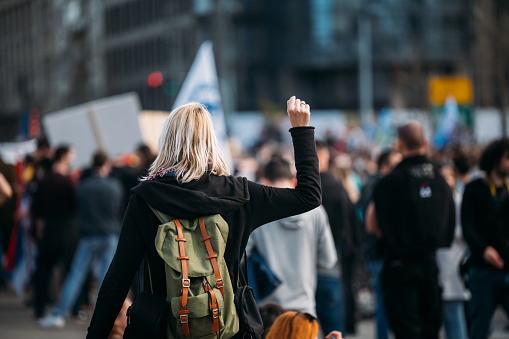 Young woman with a raised fist protesting in the street in front of the government building.\n2021