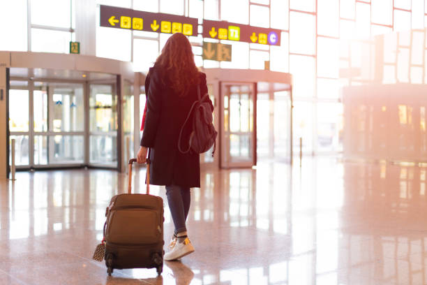 widok z tyłu brunetka kobieta wyjście z lotniska z wózkiem (bagaż podręczny) - airport zdjęcia i obrazy z banku zdjęć