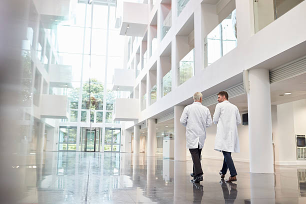 rear view of doctors talking as they walk through hospital - lobby stockfoto's en -beelden