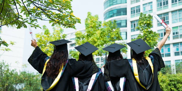 Rear view of four female graduates wearing graduation caps and gowns at campus Rear view of four female graduates wearing graduation caps and gowns at campus. bachelor degrees stock pictures, royalty-free photos & images