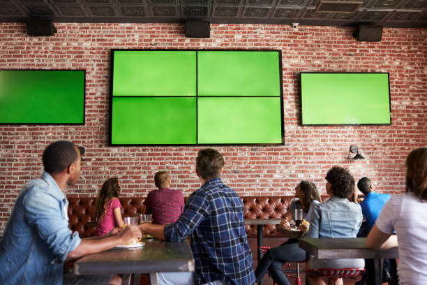 Rear View Of Friends Watching Game In Sports Bar On Screens Rear View Of Friends Watching Game In Sports Bar On Screens match sport photos stock pictures, royalty-free photos & images