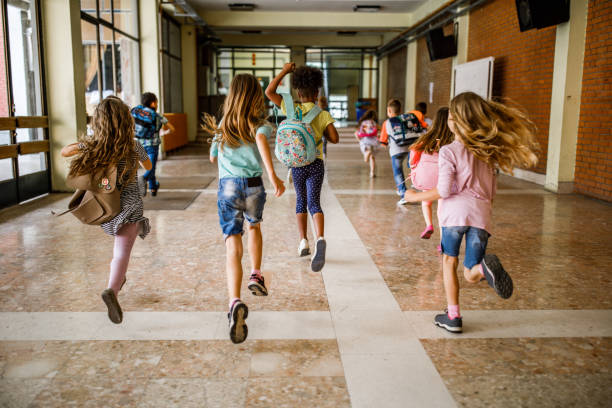 Rear view of group of school children running down the hallway. Back view of elementary students running in the school hallway. the end stock pictures, royalty-free photos & images
