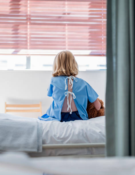 Rear view of ill girl sitting on bed in hospital stock photo