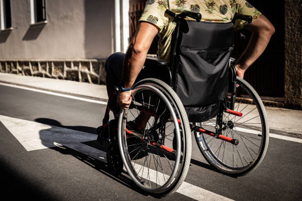 Rear view of man in wheelchair moving to his therapy in the middle of the street. stock photo