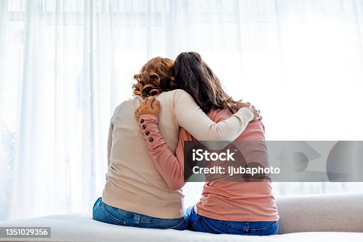 istock Rear view of mother and daughter embracing sitting on bed 1351029356