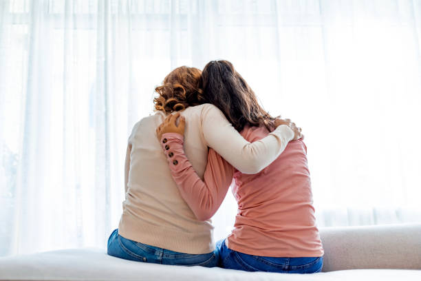 Rear view of mother and daughter embracing sitting on bed stock photo