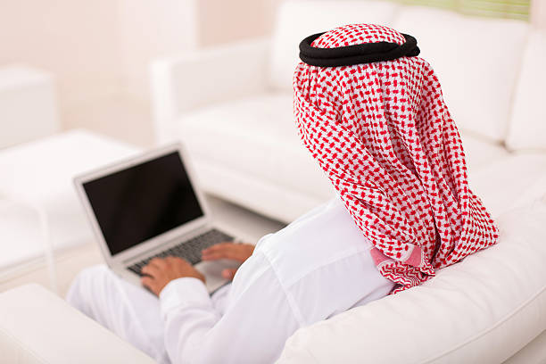 rear view of muslim man sitting on sofa rear view of muslim man sitting on sofa using laptop agal stock pictures, royalty-free photos & images