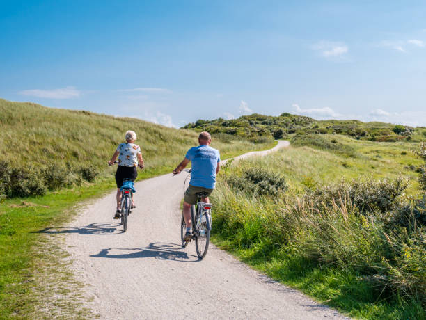 Rear view of people riding bikes on bicycle path in dunes of nature reserve Het Oerd on West Frisian island Ameland, Netherlands stock photo