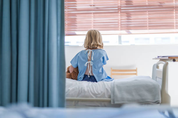 Rear view of sick girl sitting on hospital bed stock photo